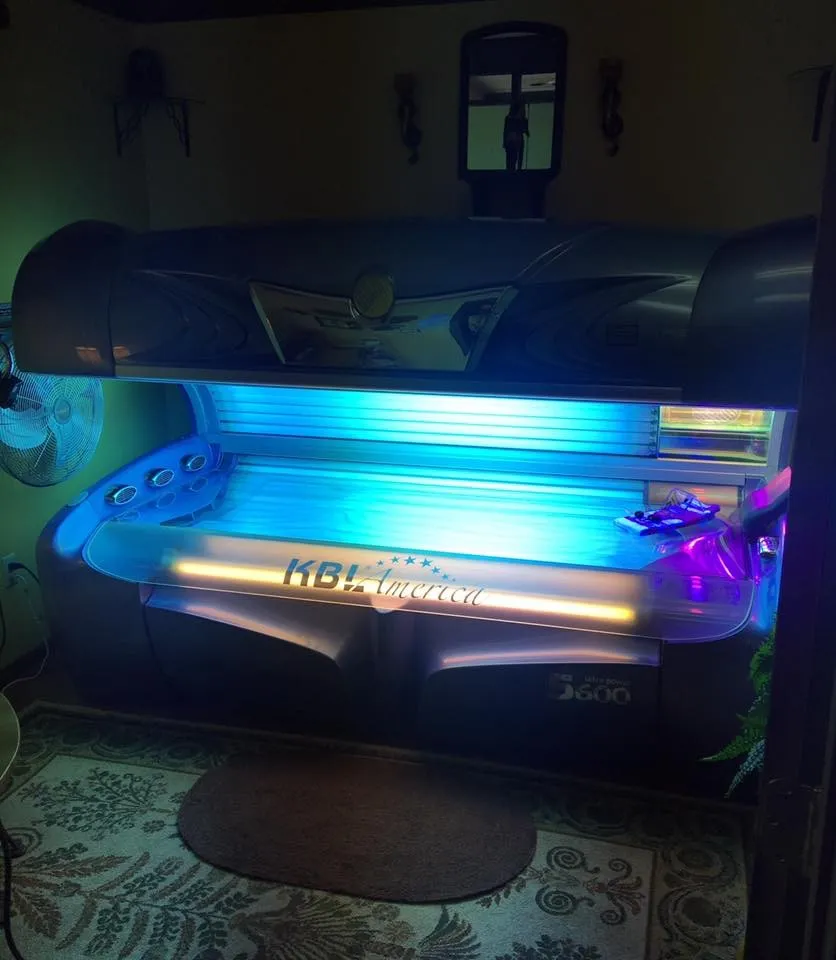 A lay-down tanning bed glowing blue in a room with a patterned rug